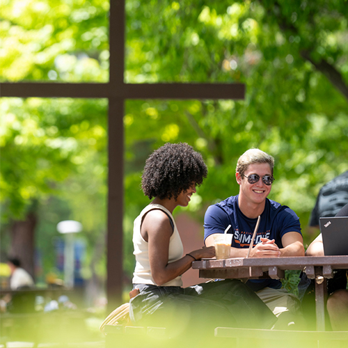 2 students sitting at a table with a cross in the background