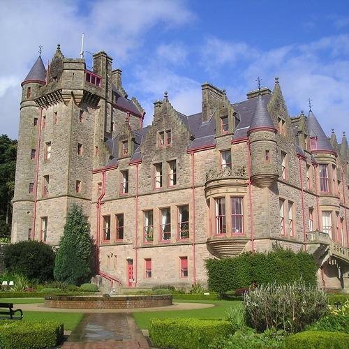 Stone castle with turrets, red-trimmed windows and landscaped gardens.