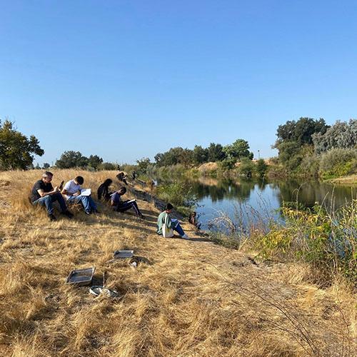 Group of students sitting and sketching by the river