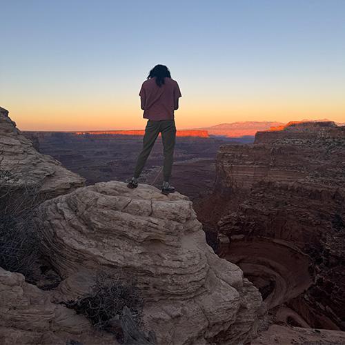 Photo of FPU student standing on a rock overlooking a sunset