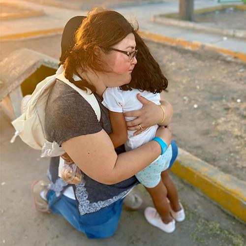 Franny kneels to embrace a child.