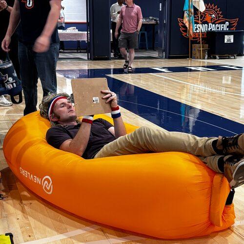 A man reclines on an orange inflatable couch while drawing on a clipboard in the FPU gym.