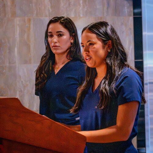 Two nursing students in navy scrubs stand together at a podium during a presentation.