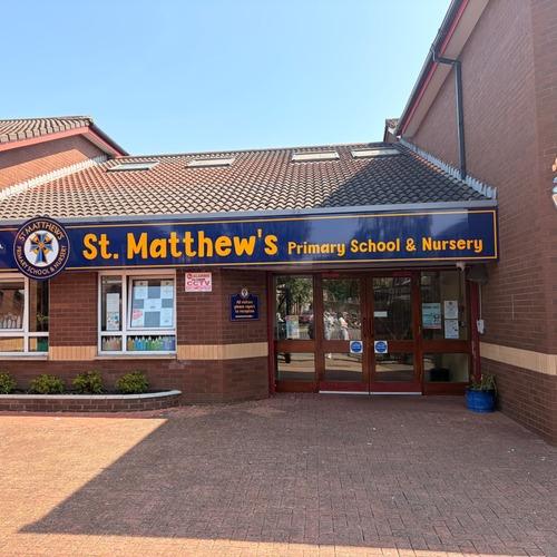 Entrance to St. Matthew’s Primary School and Nursery beneath a blue and yellow sign.