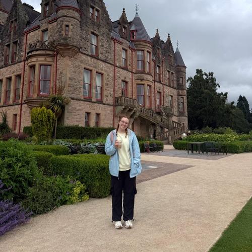 An FPU student smiles on a garden path in front of a stone castle.