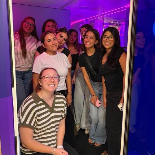 FPU students smile together in a mirrored room illuminated by purple lights.