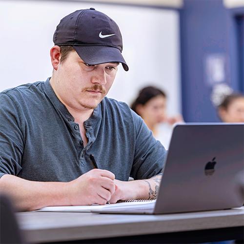College student writing on a notebook while looking at a laptop