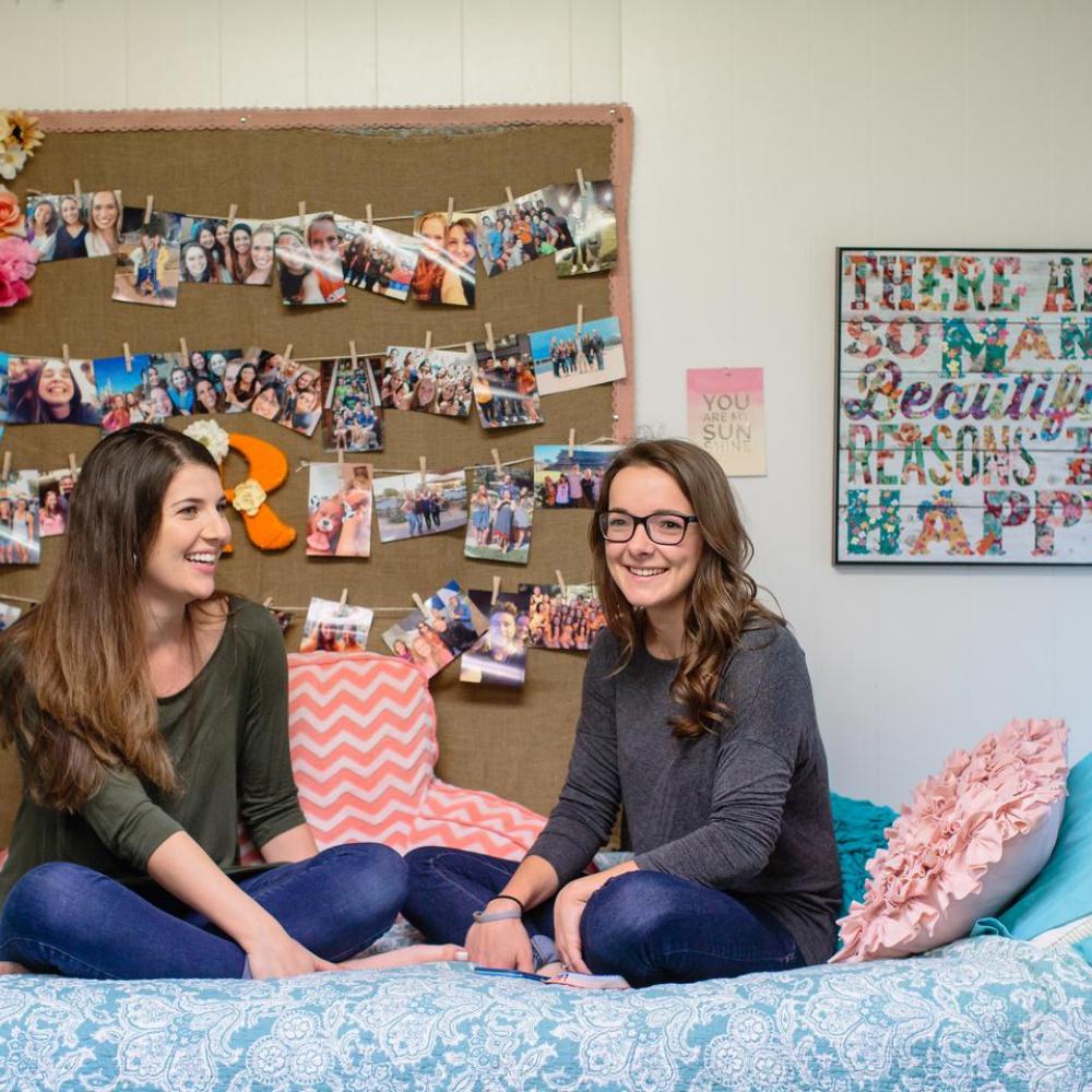 Roommates sitting on a bed in their dorm room