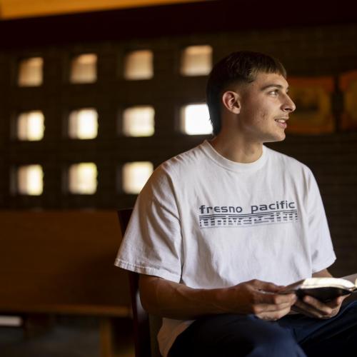 A Fresno Pacific University student sits in a chapel holding an open Bible.