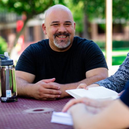 Three adult students sitting at a table outside