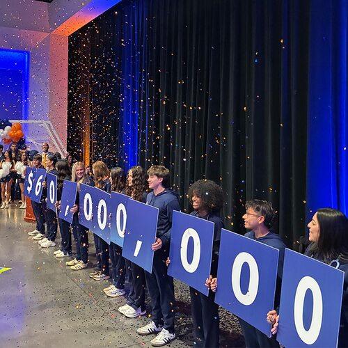 Fresno Pacific University students hold signs displaying $60 million as orange confetti falls during a campus celebration.