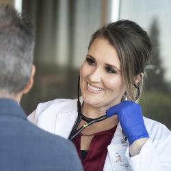 Nursing student uses a stethoscope while smiling and listening to a patient.