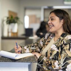A smiling woman writes on a notepad.