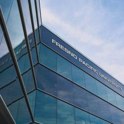 Low-angle view of Fresno Pacific University’s North Campus building with reflective blue glass and university signage.