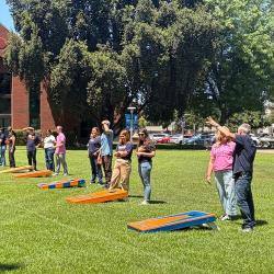 FPU community members play cornhole together on a sunny campus lawn.