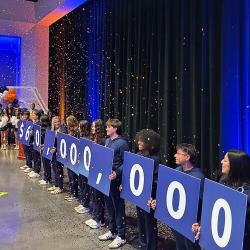 Fresno Pacific University students hold signs displaying $60 million as orange confetti falls during a campus celebration.