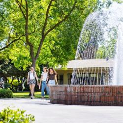 Three students walk together beside a fountain on Fresno Pacific University’s tree-lined campus.