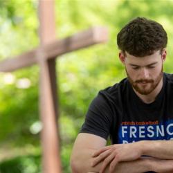 Student praying with a cross in the background.